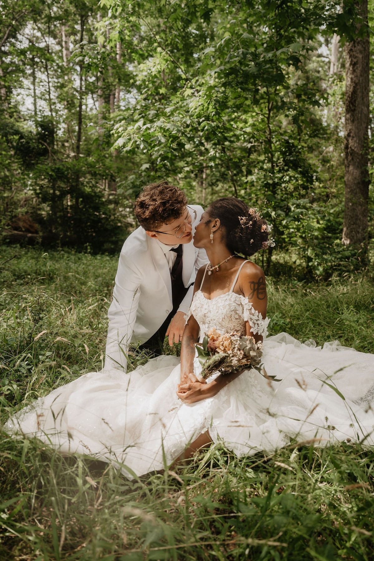 Couple sitting close together in tall grass, laughing, during golden-hour portraits in North Georgia