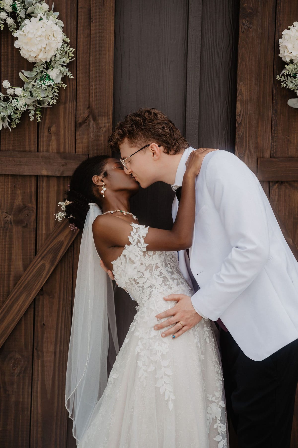 Bride and groom kissing in front of rustic wooden barn doors at their North Georgia wedding