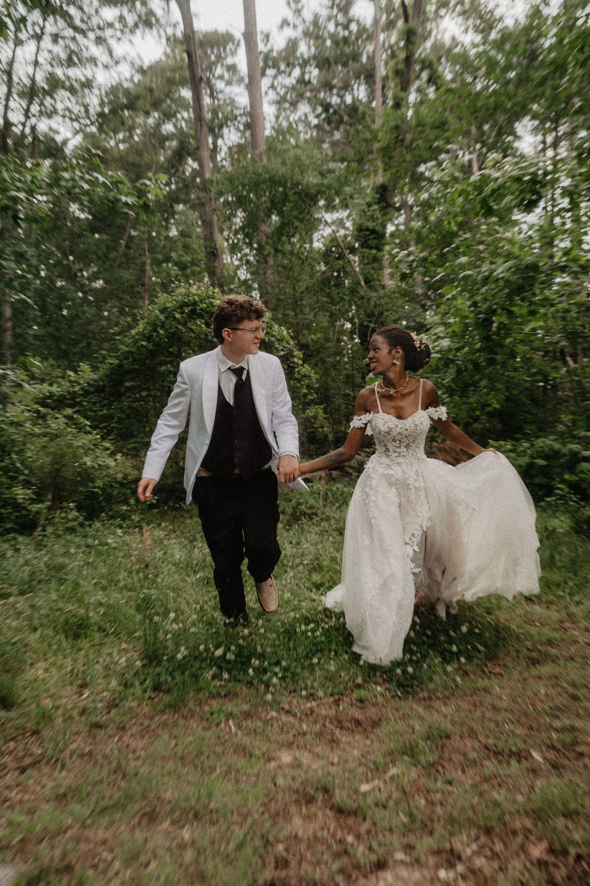 Bride and groom walking hand in hand through tall summer greenery at their North Georgia wedding